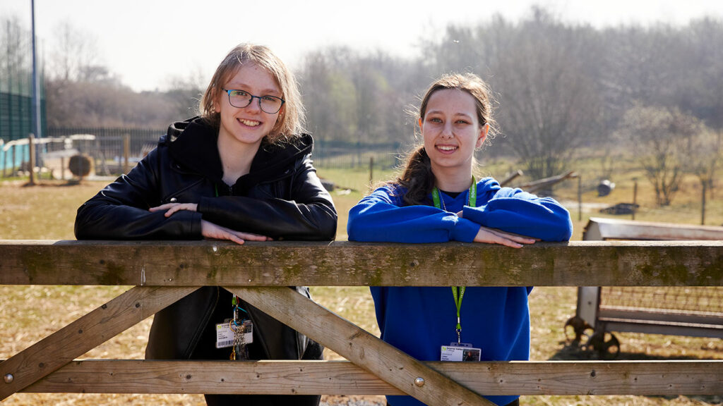Two people stood leaning on the top of a farm gate