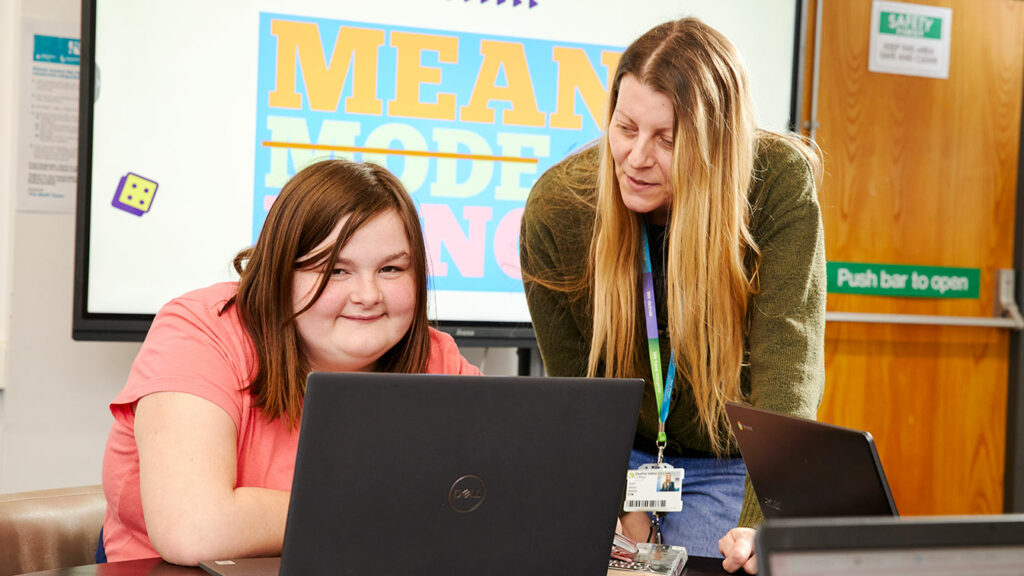 A flex student sat at a laptop with a tutor stood by them