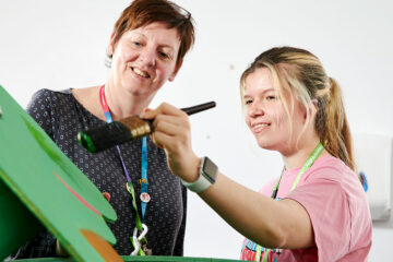 A flex student painting and a tutor stood looking on