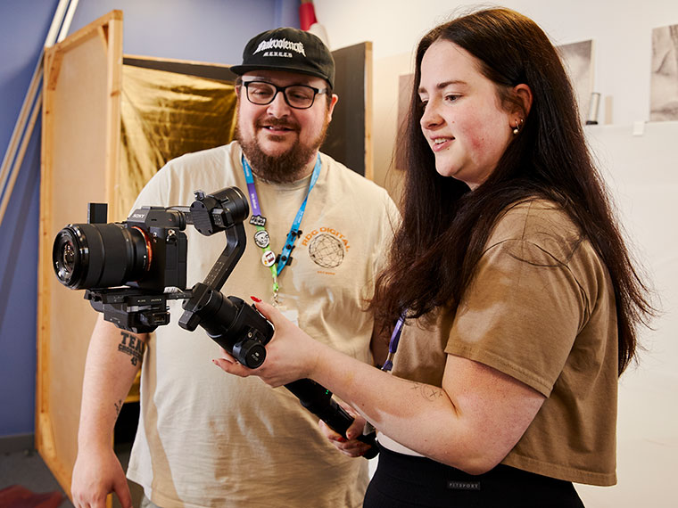 A photography student stood with a tutor looking at a camera