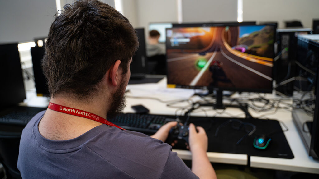 A male sat holding a controller and looking towards a screen