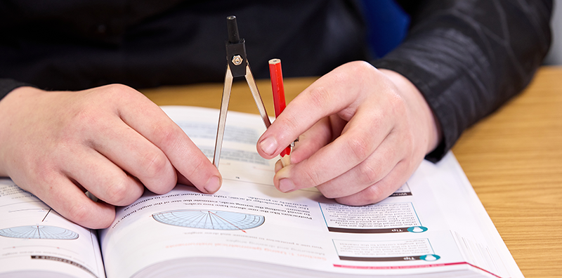 Student holding a compass on a maths workbook