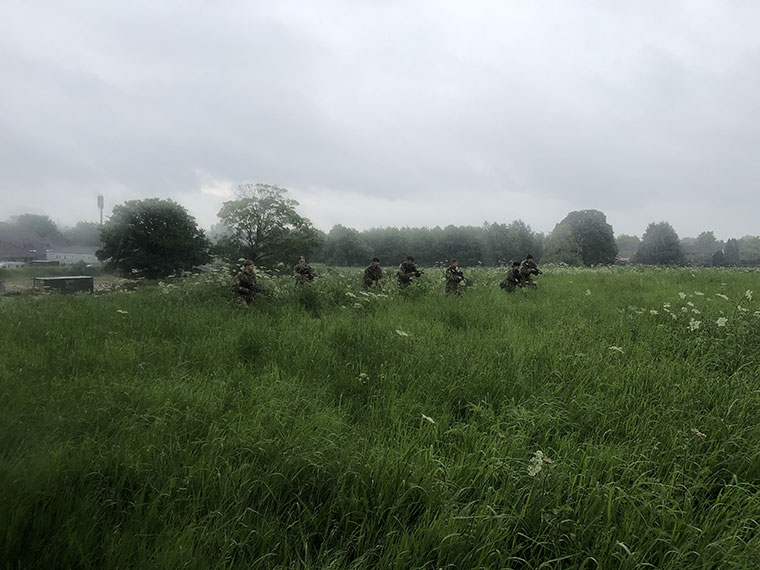 Protective Services students laying in long grass wearing army clothing