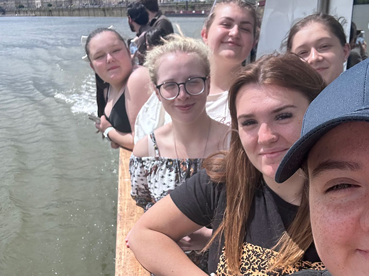 Six students on a boat leaning over the side taking a selfie