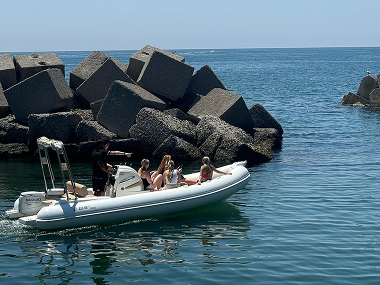 A group of students having a boat ride in the sea with large rocks in a background