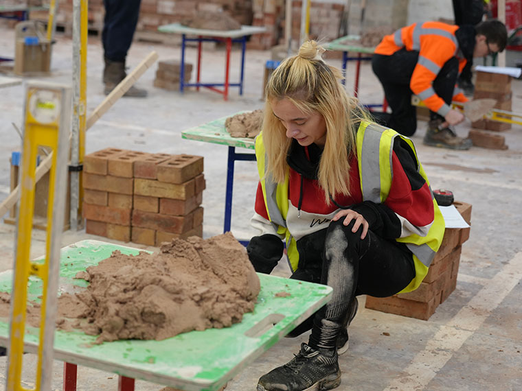 A bricklaying student knelt infront of some cement and bricks