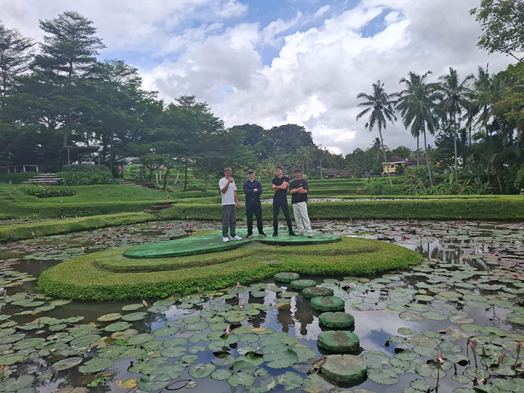 Four people stood on a grass island in the middle of a large pond with palm trees in the background