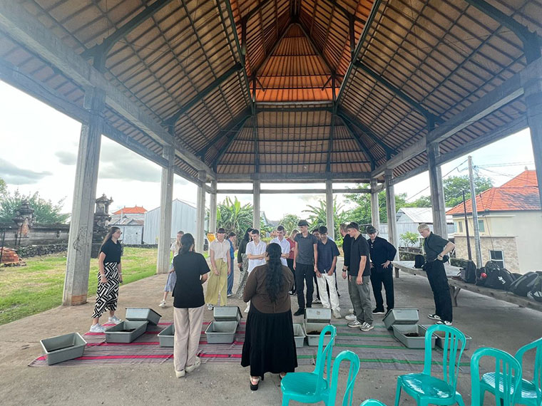 A group of people listening to someone speak, stood in front of containers of soil