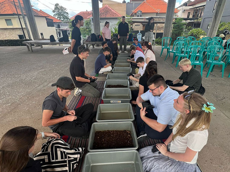 A group of people knelt down in front of containers of soil