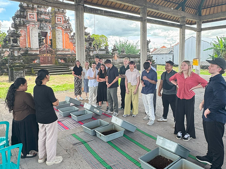 A group of people listening to someone speak, stood in front of containers of soil