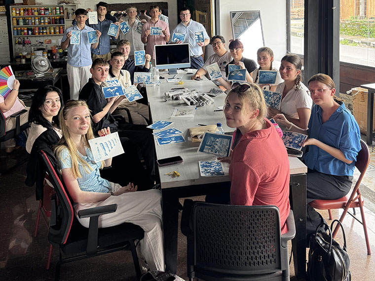 A large group of people sat around a long table working on artwork