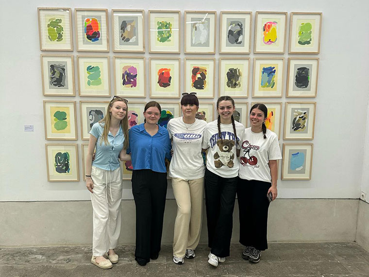 Five people stood together in front of many framed artworks hung on the wall