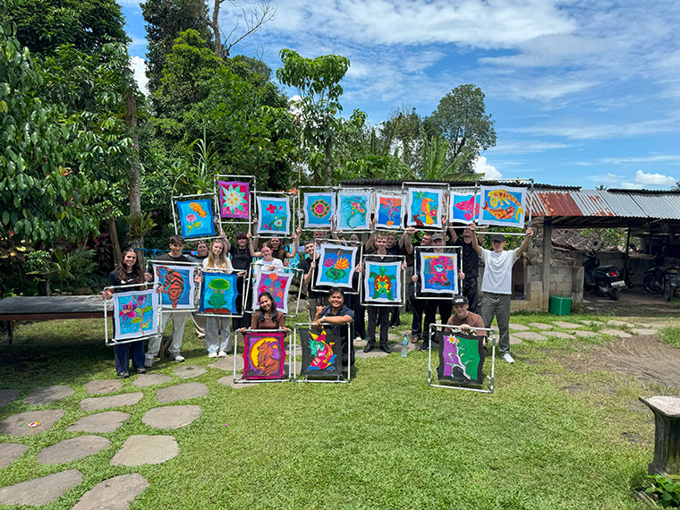 A group of people stood on grass under a blue sky holding up prints