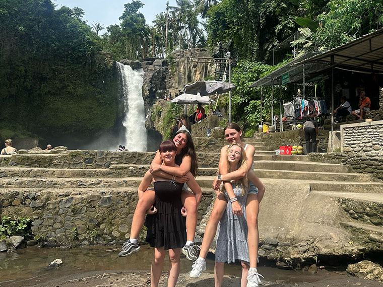 Two people giving piggybacks to their friends with the Waterfall, Bali in the background