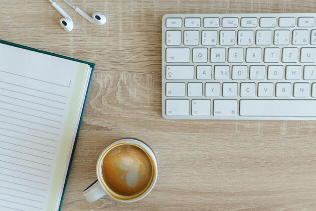 Keyboard, open notebook, ear phones and a mug
