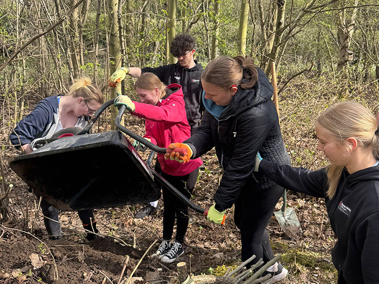 A group of students in woodland, emptying soil out of a wheel barrow