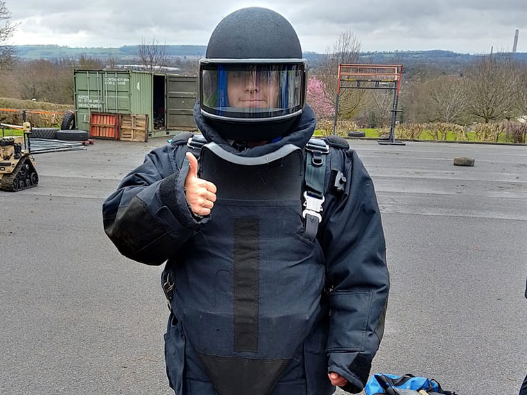 Someone stood wearing protective clothing and helmet holding their thumb up