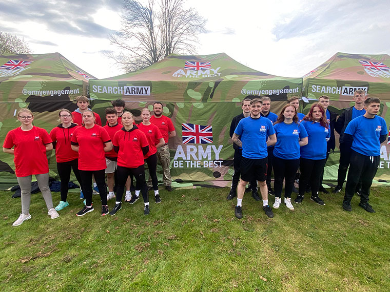 Two groups of student stood next to an army stand