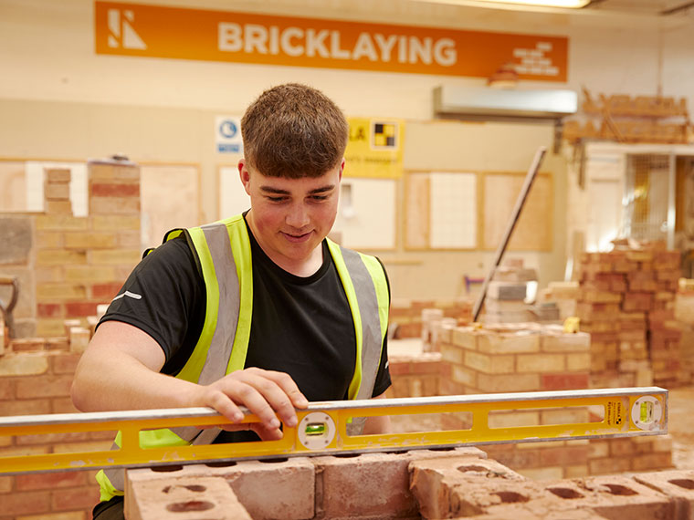 A bricklaying student placing a spirit level on top of a wall
