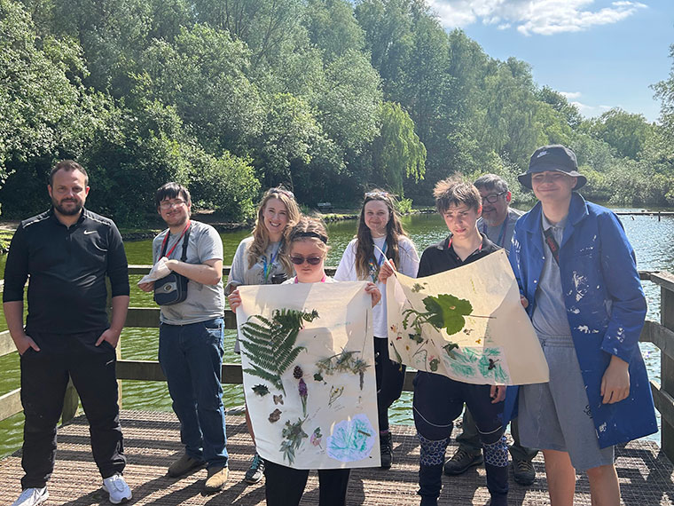 Students stood next to a lake holding their work up