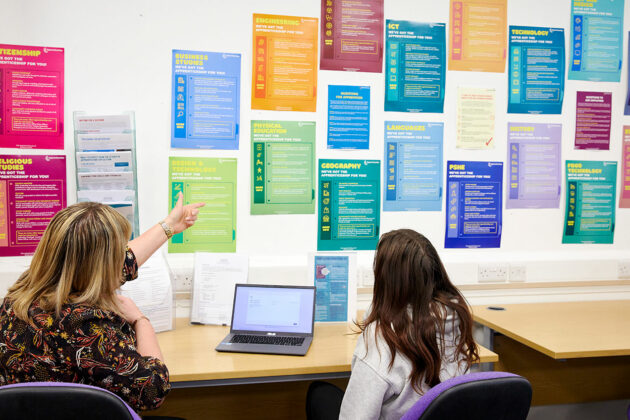 Staff speaking to a student and pointing at some information up on the wall