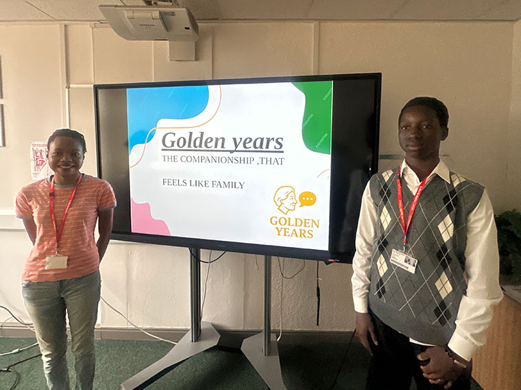 Two students stood next to a large TV screen