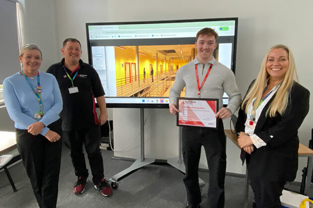 Dylan Preece stood in front of an image of his design with staff members