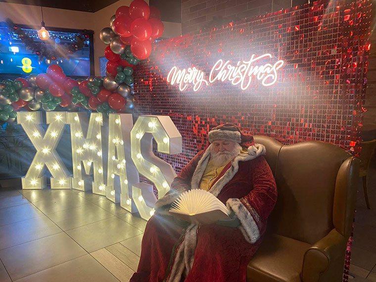 Santa sat on a chair next to large letters spelling out 'Xmas'