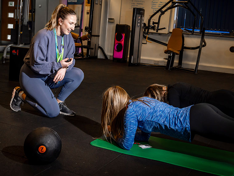 A member of staff knelt down next to two students who are doing the plank