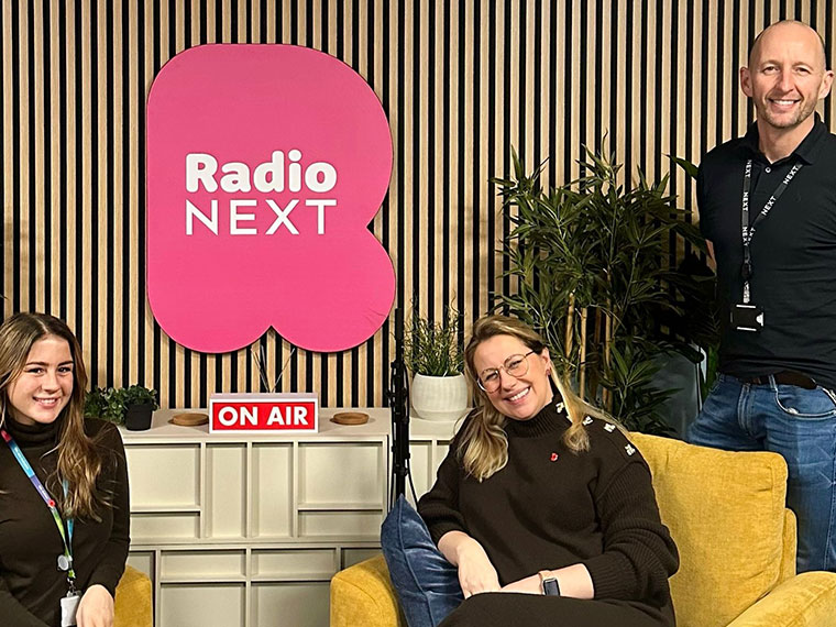 Three people smiling, in front of a Radio Next sign