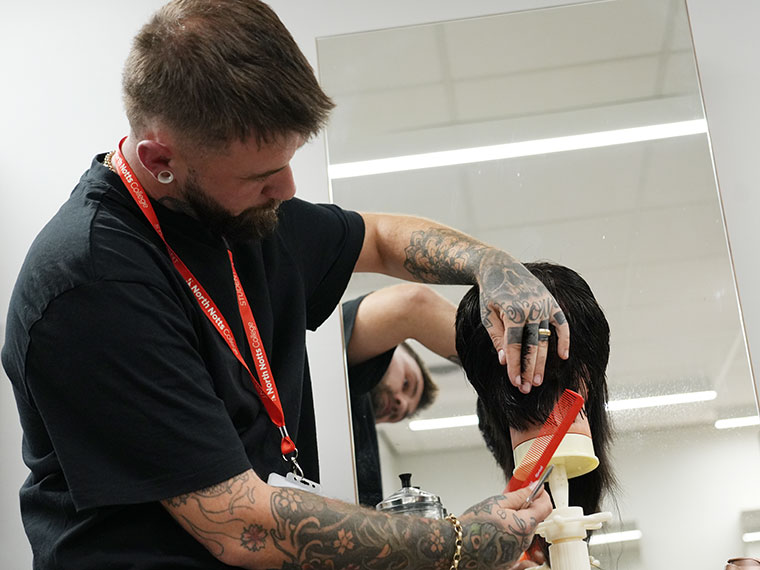 An adult learner cutting hair in the College's training salon