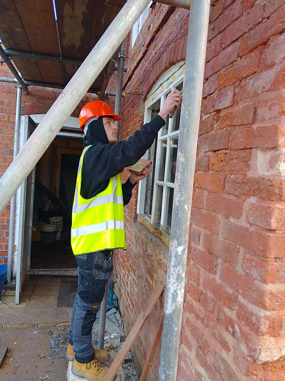 A student wearing a high vis jacket working on a window