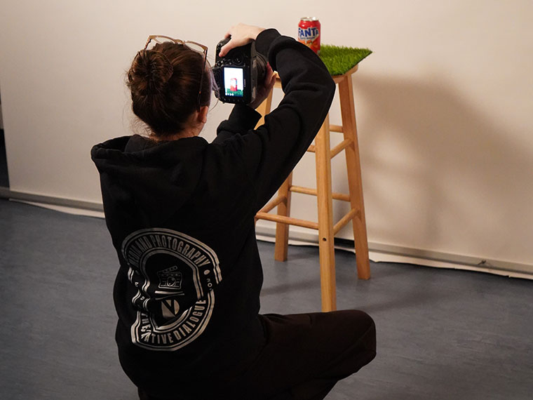 Someone bent down taking a photo of a Fanta can on a tall stool