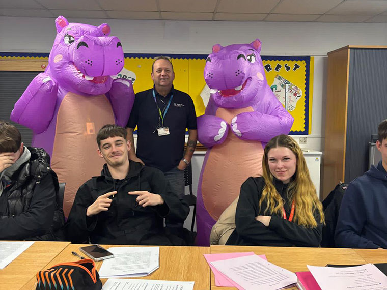 Two staff members dressed as purple hippos standing with students raising money for World Cancer Day