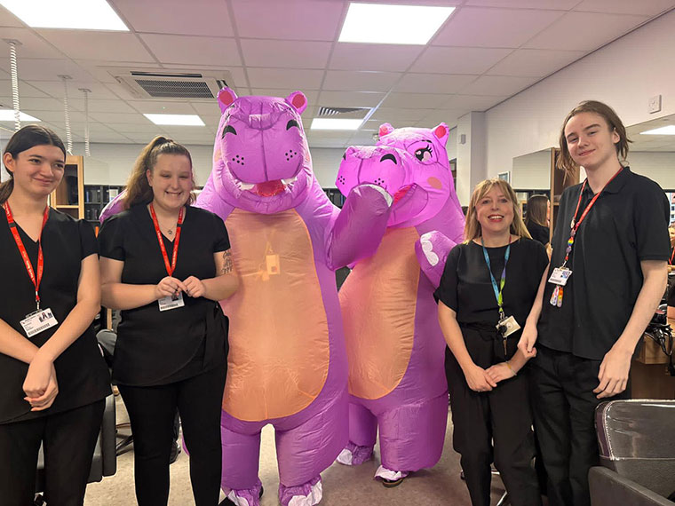 Two staff members dressed as purple hippos standing with students raising money for World Cancer Day