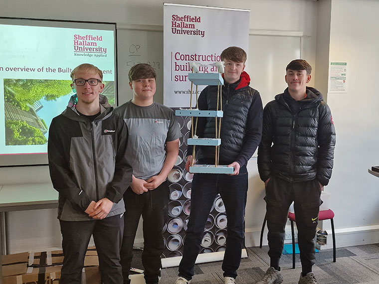 Four students stood together holding up a model
