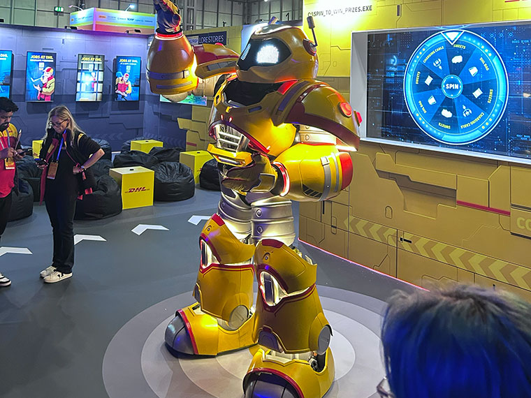 A life size yellow robot with gaming screens in the background