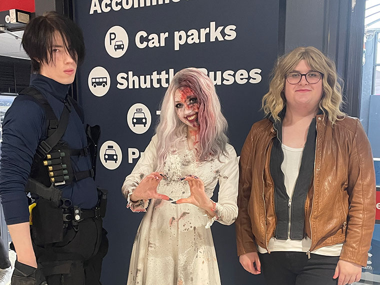 Three students dressed up, the student in the middle making a heart shape with their hands