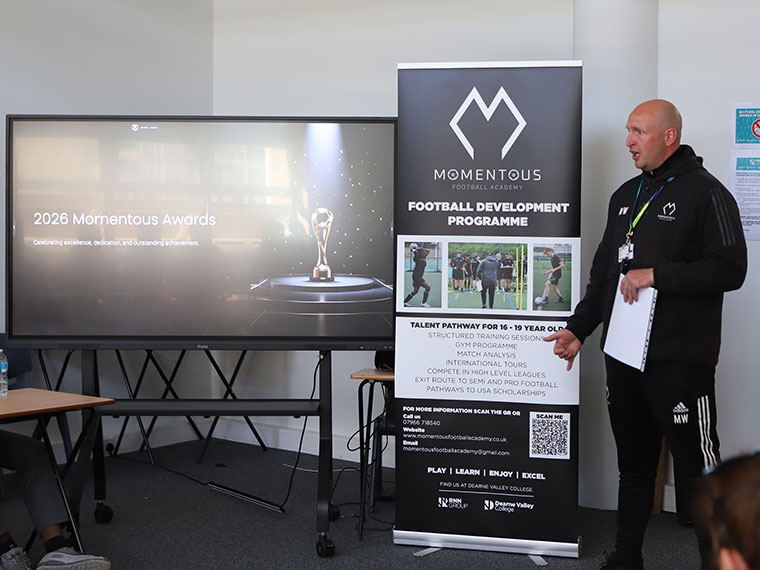A member of staff stood at the front next to a large screen presenting to an audience