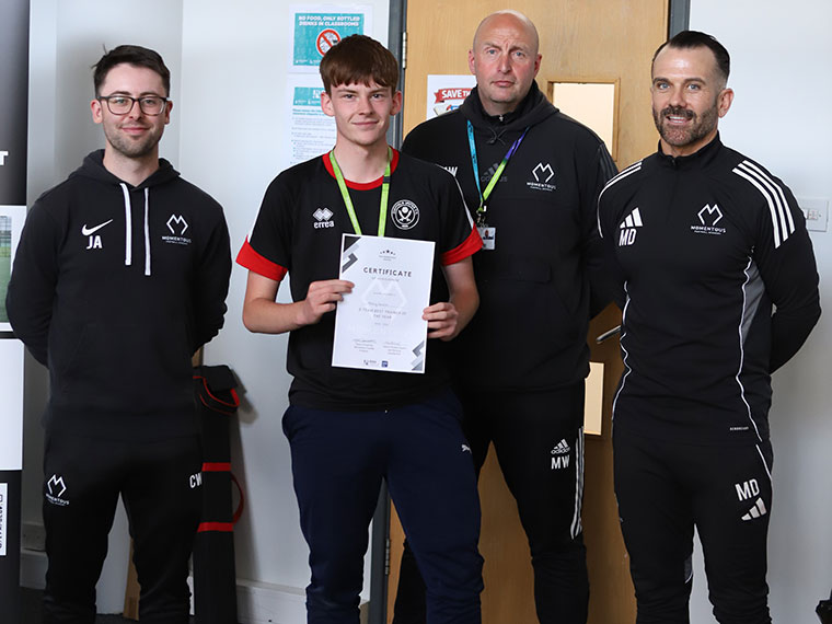 Momentous Football Academy awards winner holding a certificate stood with three members of staff