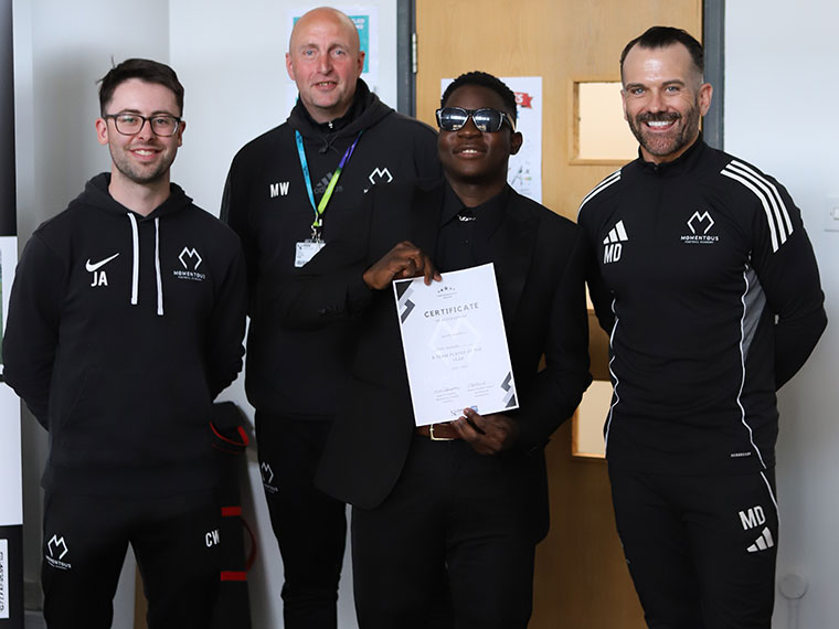 Momentous Football Academy awards winner holding a certificate stood with three members of staff