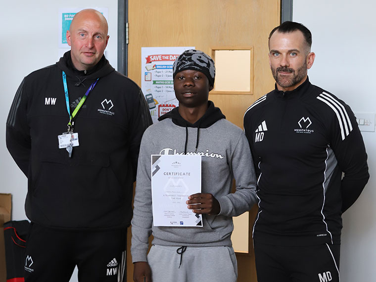 Momentous Football Academy awards winner holding a certificate stood with two members of staff