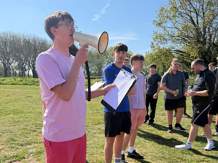 A group of students stood outside on a sunny day, one stood with a megaphone