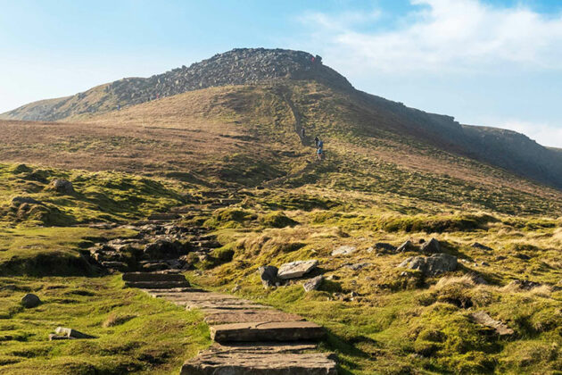 A large grassed hill with stone steps in the foreground and a blue sky