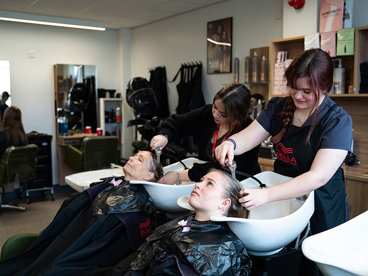 Two people stood at sinks each washing a client's hair