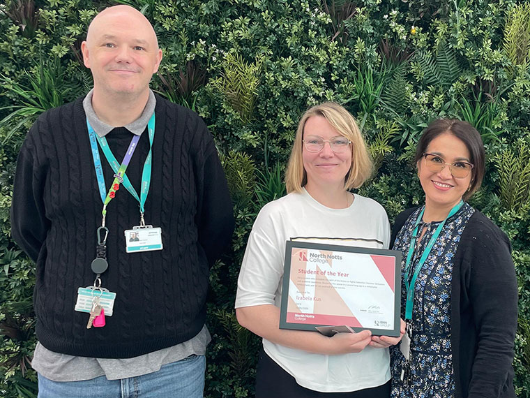 Two females and a males stood in front of a green background, the female in the middle holding a certificate
