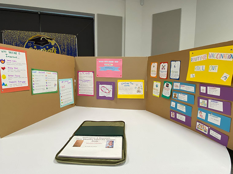 An open portfolio on a table with various pieces of work stuck up on boards around it