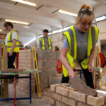 Three people bricklaying indoors wearing high vis jackets