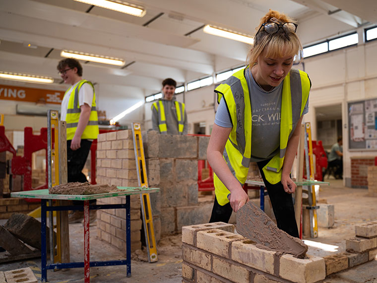 Three people bricklaying indoors wearing high vis jackets