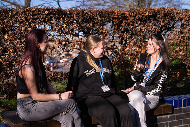 Three students sat on a wall chatting together